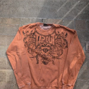 Orange långärmad tröja från Tapout - Säljer en cool orange långärmad tröja från Tapout med ett stort tryck på framsidan. Perfekt för en avslappnad stil eller träning. Tröjan är i bra skick och har en normal passform. Grym för höst och vår!