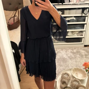 Mörkblå klänning från Chiara Forthi - Säljer en elegant mörkblå klänning från Chiara Forthi. Den har en v-ringad design med långa, transparenta ärmar och volangdetaljer på kjolen. Perfekt för festliga tillfällen! 💙