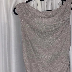 Glittrig långklänning i champagne  - Säljer en superfin glittrig långklänning i en ljus nyans. Perfekt för festliga tillfällen med sin eleganta drapering och skimrande material. Klänningen har en smickrande passform och är axelbandslös, vilket ger en stilren look. Perfekt för nyår eller andra speciella tillfällen! ✨ passar xs/s/m