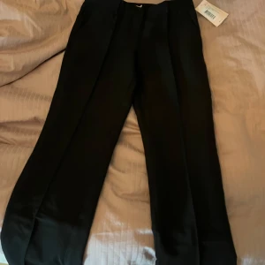 Svarta lågmidjade kostymbyxor från Nelly - Säljer ett par snygga svarta lågmidjade byxor från Nelly i storlek 36. De har en rak passform och är perfekta för både vardag och fest. Byxorna är i nytt skick med etikett kvar. Perfekt för dig som vill ha en stilren look!