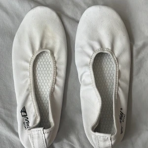 Vita gymnastikskor/dansskor  från Anniel sport - Säljer ett par vita gymnastikskor från Anniel sport. De är i bra skick och har en enkel design med elastisk öppning för enkel passform. Sulan är i beige gummi för bra grepp. Perfekta för inomhusträning eller dans.Storlek 36 eller 37