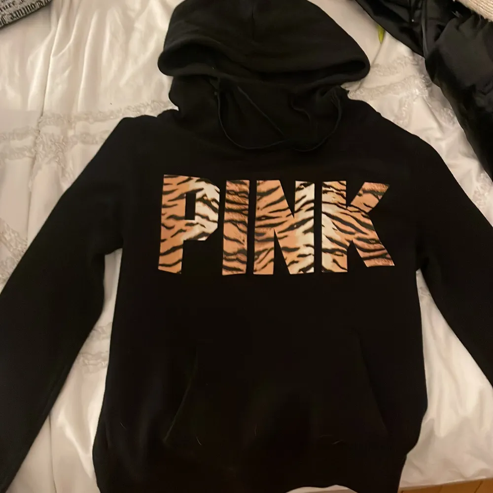 Säljer en snygg svart hoodie från Victoria's Secret PINK. Den har ett coolt tryck med ordet 'PINK' i ett zebramönster på framsidan. Perfekt för en avslappnad stil och gjord i en mjuk bomulls- och polyesterblandning. Passar perfekt för höst och vinter!. Hoodies.