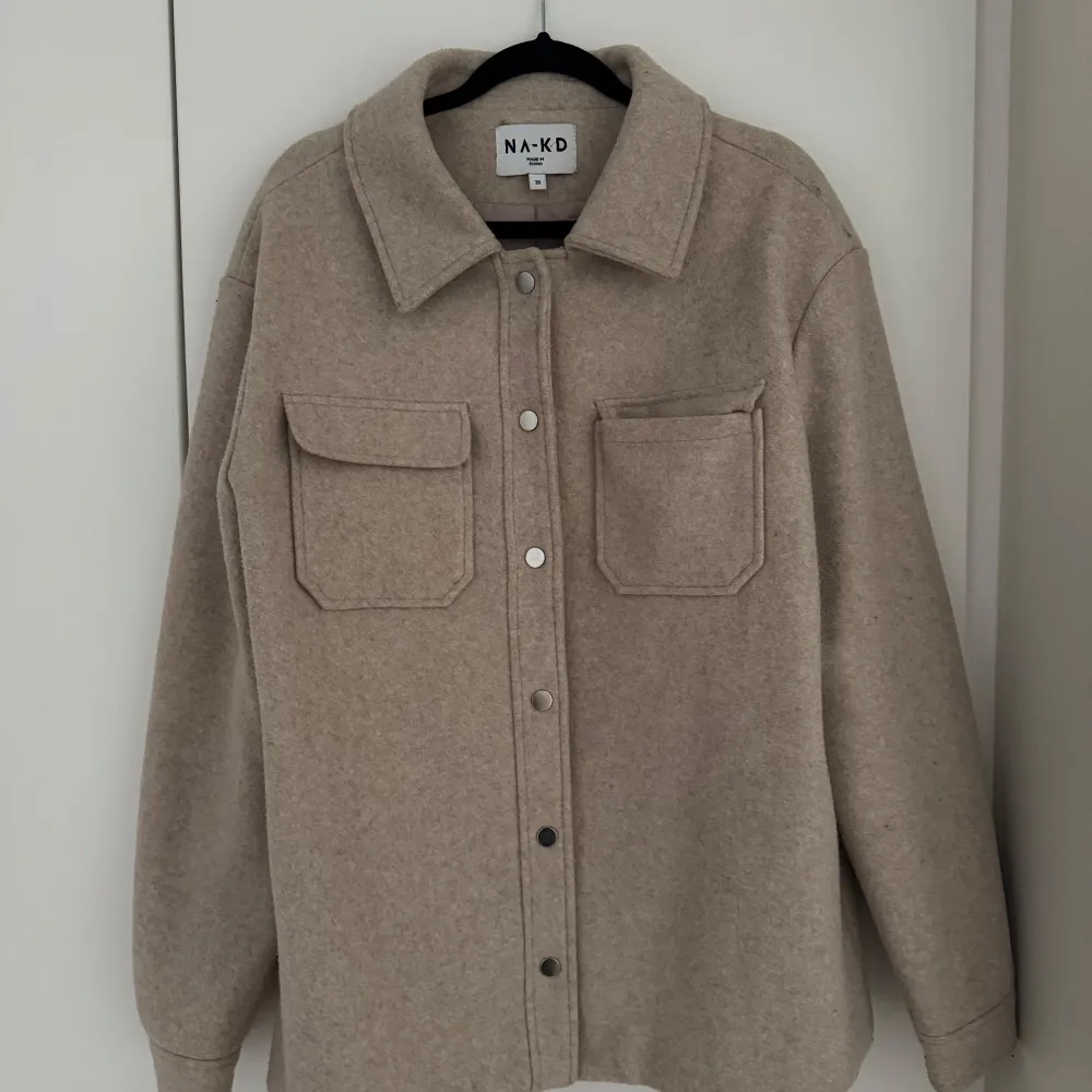 Säljer en snygg beige jacka från NA-KD i storlek 38. Den har en stilren design med knappar framtill och två praktiska bröstfickor. Perfekt för höst och vår. 🧥✨ . Takit.