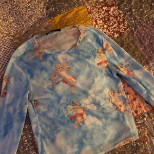 Blå långärmad topp med änglamotiv  - Säljer en superfin blå långärmad topp från Shein med ett unikt änglamotiv. Perfekt för dig som vill ha något annorlunda i garderoben! Toppen är i ett lätt och bekvämt material, perfekt för vår och sommar. Genomskinligt mesh matrial