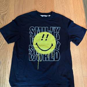 Svart Smiley world T-shirt säljes. På tröjan är det en gul smiley och det står smiley world. Tröjan är bara provad men aldrig använd. Storlek 170