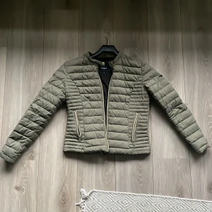 Olivgrön pufferjacka från Rockandblue - Säljer en snygg olivgrön pufferjacka från Rockandblue i storlek 36. Jackan har en dragkedja framtill och är quiltad för extra värme. Perfekt för höst och vår! Den är i mycket bra skick och har en stilren design som passar till det mesta. 🧥🍂