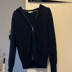 Mörkblå hoodie från Soft Goat - Säljer en mörkblå hoodie från Soft Coat i bra skick. Den har en dragkedja framtill och en luva med snören. Perfekt för höst och vår när du vill ha något bekvämt och stilrent. Passar till både vardag och chill.