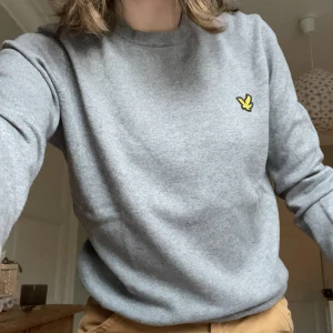 Grå tröja från Lyle & Scott - Säljer en stilren grå tröja från Lyle & Scott i mycket bra skick. Den har en klassisk design med rund hals och ett gul fågel på bröstet. Perfekt för både vardag och lite finare tillfällen. Superbekväm och lätt att matcha med olika outfits! Säljer även en blå och en mörk mörk blå. 