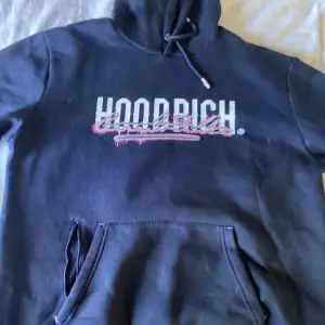 Säljer en svart hoodie från Hoodrich i storlek XL. Den har en stor ficka fram och en snygg logga i vitt och rosa på bröstet. Perfekt för en avslappnad stil eller att mysa i hemma. Huvan har dragsko för justering. Hör av dig vid intresse!