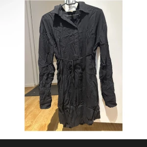 Svart klänning från H&M Mama - Snygg svart klänning från H&M Mama i storlek XS. Perfekt för både vardag och fest med sin stilrena design. Klänningen har långa ärmar och ett bälte i midjan för en smickrande passform. Materialet är mjukt och bekvämt, vilket gör den idealisk för alla tillfällen.
