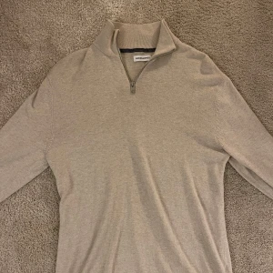 Beige tröja från Jack & Jones - Säljer en stilren beige tröja från Jack & Jones. Den har en dragkedja vid halsen och är långärmad, perfekt för kyliga dagar. Tröjan är i bra skick och passar både till vardags och lite finare tillfällen. Skön och enkel att matcha med andra plagg! Skick 9,5/10