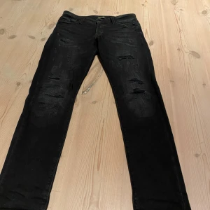 Svarta Jack&jones jeans med slitningar - Säljer ett par svarta jeans i bra skick med feta slitningar på framsidan. De har en normal passform och är perfekta för en avslappnad stil. De är i mycket bra skick.                                         Storlek W30/L32. Nypris 800 kr🤩
