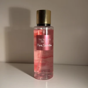 Victoria's Secret Pure Seduction Mist - Säljer en fräsch och blommig doftmist från Victoria's Secret, Pure Seduction. Flaskan är genomskinlig med rosa vätska och har en elegant guldlock. Doften har inslag av plommon, fresia och kamomill. Perfekt för daglig användning eller speciella tillfällen. Flaskan rymmer 250 ml.