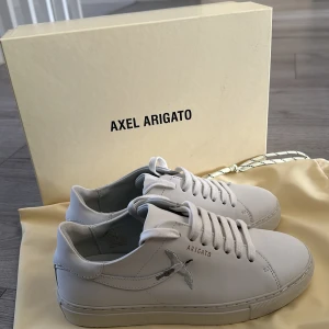 Vita sneakers från Axel Arigato - Säljer ett par stilrena vita sneakers från Axel Arigato i mycket bra skick. Skorna har en snygg fågelbrodering på sidan och klassisk snörning. Perfekta för både vardag och fest! 🕊️