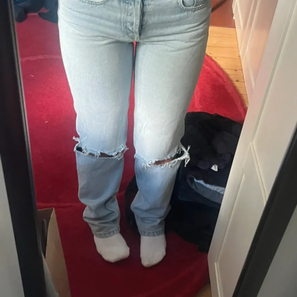 Säljer ett par ljusblå jeans med hål/slitningar vid knäna. De är mid waist och har en straight passform. Lite slita längst ned men det syns knappt.. Jeans & Byxor.