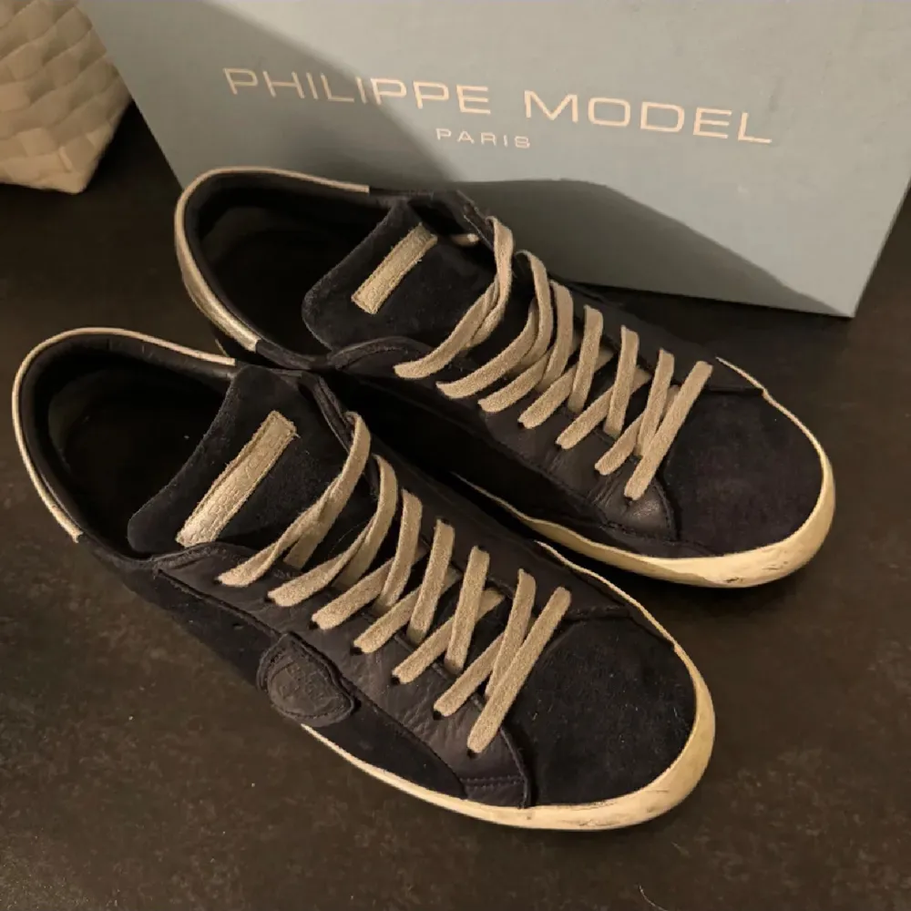 Säljer ett par snygga svarta sneakers från Philippe Model i bra skick. De har en klassisk design med grå snörning och en vit sula. Perfekta för både vardag och festliga tillfällen. Skorna är bekväma och stilrena, ett måste i garderoben!. Skor.