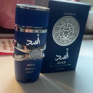 lattafa Asad Zanzibar - Säljer en elegant Asad Zanzibar parfym från Lattafa. Flaskan är djupblå med silverdetaljer och har en stilren design. Förpackningen har ett snyggt mönster och arabiska inskriptioner. Perfekt för den som vill ha en unik och lyxig doftupplevelse. 99ml kvar. Säljer det då jag har gott om summar parfymer. Priset kan diskuteras!