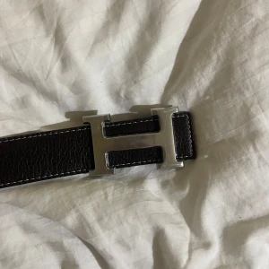 Svart skärp med silverfärgat spänne - Snyggt svart skärp i skinn med ett stilrent silverfärgat H-format spänne. Perfekt för att ge en elegant touch till din outfit.