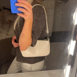 Silvrig axelväska med krokodilmönster - Snygg silvrig axelväska i syntetmaterial med krokodilmönster. Väskan har en praktisk dragkedja upptill och en justerbar axelrem. Perfekt för både vardag och fest! 🐊✨