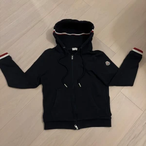 Moncler cardigan/hoodie - Säljer en snygg Moncler hoodie i navy blue. Den är i mycket fint skick utan defekter och har en fungerande NFC Scan samt qr-kod. För mer bilder eller frågor, kontakta mig!☺️Pris kan diskuteras🙂