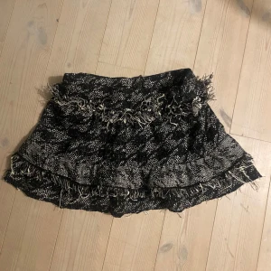 Svart och vit kjol från Zara Woman - Trendig svart och vit kjol från Zara Woman med fransiga detaljer och dragkedja. Kjolen har ett unikt mönster och volangkant som ger en chic look. Perfekt för att ge din outfit en edgy touch.