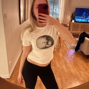 Vit t-shirt med discokultryck - Snygg vit t-shirt med ett stort discokultryck på framsidan. Perfekt för en festlig look! T-shirten har en normal passform och korta ärmar. Köpt på Plick, vet inte var den är från då den saknar lapp.