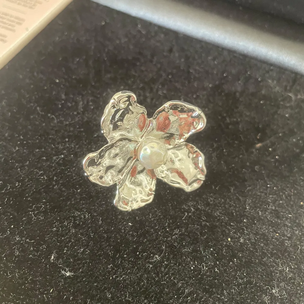 Elegant ring i form av en blomma med en vacker pärla i mitten. Den silverfärgade designen ger en stilren och tidlös look, perfekt för att lyfta vilken outfit som helst.. Asusteet.
