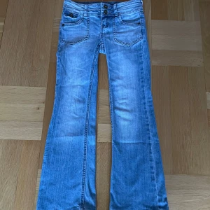Blå bootcut jeans - Snygga blå bootcut jeans med låg midja och dubbla knappar fram. Jeansen har dekorativa sömmar på bakfickorna och en klassisk femficksdesign. 