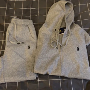 Grå Ralph Lauren zip hoodie och matchande byxor - Säljer en stilren grå hoodie från Ralph Lauren med dragkedja och klassisk logga på bröstet och gråa matchande byxor. Säljer för de va för små för mig men riktigt sköna och snygga. Har inte använt mer än testat.