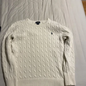 Vit stickad tröja från Polo Ralph Lauren - Säljer en klassisk vit stickad tröja från Polo Ralph Lauren med kabelstickat mönster. Tröjan har långa ärmar och en broderad logotyp på bröstet. Perfekt för kyligare dagar. Storlek L för barn, passar som storlek S (herr). Skriv gärna om du har frågor angående vad som helst 