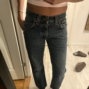 Blå jeans från Nudie Jeans - Säljer ett par klassiska blå jeans från Nudie Jeans. De har en rak passform och är tillverkade i slitstarkt denim. Byxorna har orange sömmar och en läderpatch med logotyp baktill. Perfekta för en avslappnad stil.