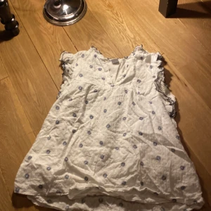 Vit blus med blommönster från Lindex - Söt vit blus från Lindex med små blommor i blått och volangdetaljer vid ärmarna. Perfekt för en somrig look!