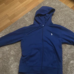 Blå hoodie från Polo Ralph Lauren - Säljer en snygg blå hoodie från Polo Ralph Lauren med dragkedja. Har använt den några gånger bara så den är i bra skick och är i storleken S