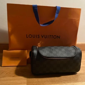 Svar necessär från Louis Vuitton - Snygg svart axelväska från Louis Vuitton med klassiskt rutigt mönster. Väskan har en praktisk dragkedja och är perfekt för att bära dina nödvändigheter med stil. Kan garantera äktahet säljes pga onödigt köp och knapp användning. Hör av er vid frågor, tack!