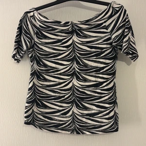 Svartvit mönstrad topp - Snygg svartvit topp med ett iögonfallande mönster. Toppen har korta ärmar och en bekväm passform. Perfekt för att ge en stilren touch till din outfit.