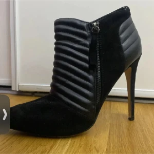 Svarta stövletter med dragkedja - Snygga svarta stövletter med hög klack och dragkedja på sidan. Skorna har en quiltad design som ger en trendig look.