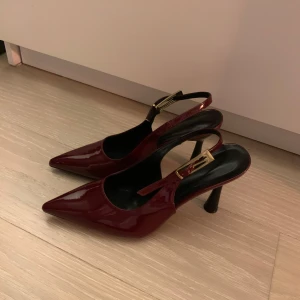 Vinröda pumps med klack storlek 38&39 - Olika storlek! 38&39. Snygga vinröda pumps med spetsig tå och hög klack. Skorna har en elegant rem med gulddetalj som ger en lyxig känsla. Perfekta för att lyfta vilken outfit som helst. Endast testade. Råkade få en i fel storlek när jag beställde och leverantören ville inte ha tillbaka dem. Vänster är strl. 39 och höger 38. 