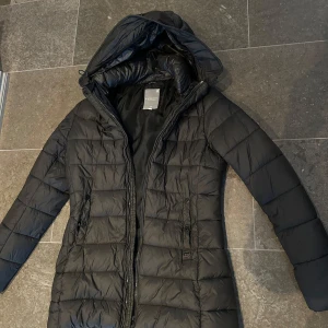 Mörkgrön dunjacka från G-Star - Säljer en svart dunjacka från G-Star med huva och dragkedja. Jackan är perfekt för kyliga dagar och har en stilren design med quiltade detaljer. Den går precis över rumpan (på mig som är 174 lång) och är fin form på (lite mer slim fit) Står storlek M i den men jag är en klassisk S och den är lite tajt på mig så passar perfekt till en XS. 