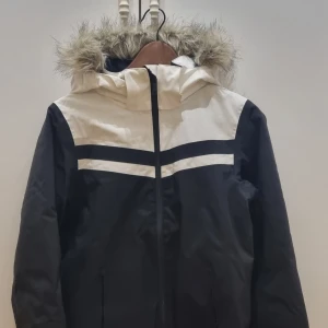 Svart och vit jacka skidjacka från Everest - Snygg svart och vit jacka från Everest med pälskrage och dragkedja, snölås i midja 9ch ärmslut. Perfekt för kyliga dagar i skidbacken med sin stilrena design och praktiska huva.