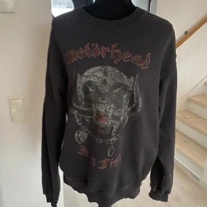 Svart Motörhead sweatshirt - Cool svart sweatshirt med Motörhead-tryck på framsidan och turnélista från Iron Fist Tour 1982 på baksidan. Tröjan har långa ärmar och rund halsringning. Perfekt för fans av klassisk rock!