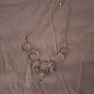 Antikt halsband med blå stenar - Unikt antikt halsband med dekorativa cirklar och blå stenar. Kedjan är i en antik stil och stenarna ger en elegant touch. Perfekt för att ge en vintage känsla till din outfit.