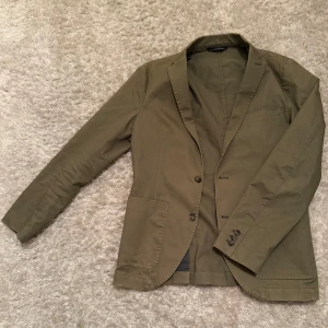 Olivgrön kavaj från Matinque - Snygg olivgrön kavaj från Matinique med två knappar framtill och klassisk krage. Perfekt för en stilren look. Kavajen har en innerficka och är helfodrad med ett randigt mönster.