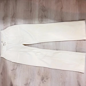 Vita mjukisbyxor från Juicy Couture - Säljer ett par vita nya oanvända mjukisbyxor från Juicy Couture i stl M. Byxorna har en bekväm passform med elastisk midja och praktiska fickor med knappar. Perfekta för en avslappnad stil.