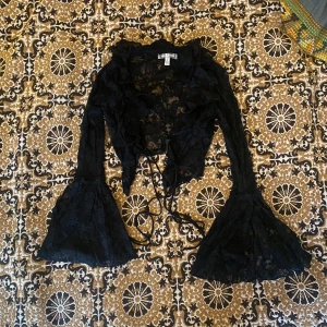 Svart spetsblus från Urban Outfitters med utsvängda ärmar!! - Så snygg blus i spets och utsvängda ärmar. Den går att knyta framtill