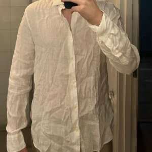 Vit linneskjorta Riley - Snygg och luftig vit linneskjorta med knappar framtill. Perfekt för varma dagar med sin lätta och andningsbara design. Skjortan har långa ärmar och en klassisk krage.