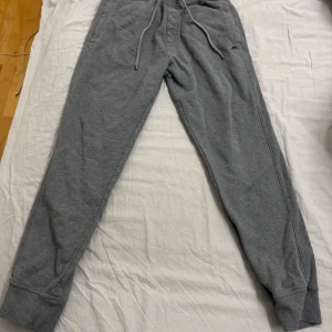 Grå mjukisbyxor med snörning - Säljer ett par grå mjukisbyxor med snörning i midjan. Byxorna har en avslappnad passform och är perfekta för en bekväm dag hemma. De har ribbade muddar vid bensluten och en liten logga på ena benet. Detta är ett par J Lindberg mjukisbyxor och ordinarie pris ligger på 700kr, men säljer de för 350kr istället. Jag har använt dem minst 10 gånger, men jag tyckte inte om dem riktigt så jag säljer dem. Pris kan diskuteras om det är så ni vill.