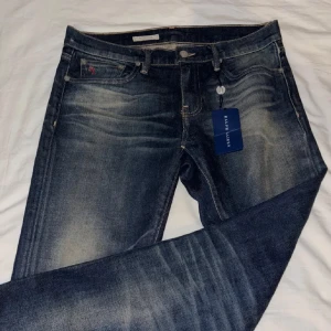 Blå jeans från Ralph Lauren - Snygga blå jeans från Ralph Lauren med en klassisk femficksdesign och subtila slitningar. De har en knappgylf och märkesdetaljer på fickan. Perfekta för en stilren look.