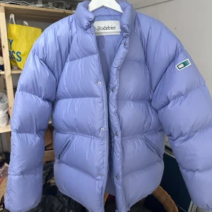 Ljuslila pufferjacka från Rodebjer - Säljer en snygg ljuslila pufferjacka från Rodebjer. Jackan har en quiltad design med en broderad detalj på ärmen. Perfekt för kyliga dagar med sin långa ärm och bekväma passform. Nypris 5995kr 