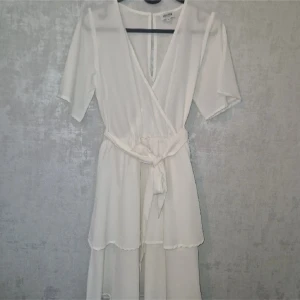 Vit omlottklänning med knytband - Säljer nu min studentklänning, använd en gång som då var på min student.  I mycket fint skick, finns en liten defekt (se sista bild) från en säkerhetsnål, syns knappt🌼 Klänningen kommer från bubbelroom och är i storlek 36,  Pris går alltid och diskutera😊