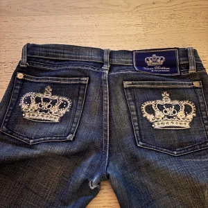 Victoria Beckham jeans - Snygga mörkblå jeans från Victoria Beckham med unika broderade kronor på bakfickorna. Jeansen har en klassisk bootcut-stil och är low waist (lågmidjade). De har ett väldigt litet hål nedanför kedjan, som man även ser på bilden jag la ut! Men eftersom hålet är såå litet kan man bara sy ihop de själv eller lämna in hos skräddaren. Midjemåttet rakt över: 38cm. Benlängden rakt ner: 97cm💕💕